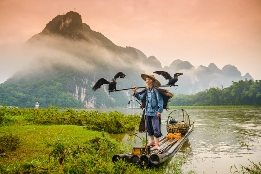 pescador de cormorán en una lancha en el rio yangshuov con montañas de fondo